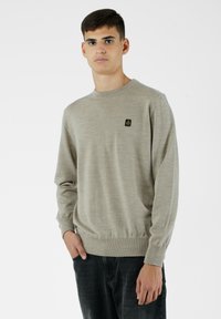 Maglione beige chiaro realizzato in morbido tessuto a maglia, con scollatura rotonda, maniche lunghe e un'etichetta nera piccola sul petto.