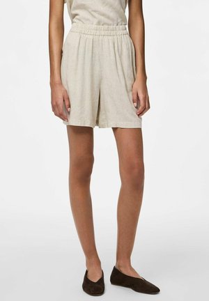 Pantaloni corti in lino di un beige chiaro con elastico in vita, vestibilità ampia e taglio al ginocchio; indossati con scarpe scivolate di un marrone scuro.