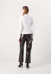 Weißer, flauschiger Pullover kombiniert mit dunkelburgunderfarbenen, glänzenden Hosen mit roten Nahtdetails, abgerundet mit schwarzen, hohen Stiefeln.