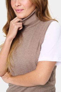 Barna bordás garbós pulóver, amely illeszkedő fazonú, fehér rövid ujjú ingre rétegezve, sima szövettextúrát mutat.