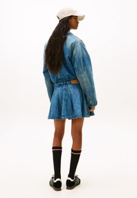 Chaqueta vaquera con cintura ajustada, combinada con una minifalda vaquera plisada. Medias negras hasta la rodilla con rayas rosas y zapatillas negras completan el conjunto.