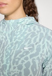 Nike kapućna jakna u svijetloj mentol boji s suptilnim uzorkom u motivu životinja, koja ima zatvaranje na zip i detalj logotipa u bijeloj boji na prsima.