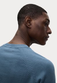 Helles blaues Strickpullover mit Rundhalsausschnitt, strukturiertem Nähen entlang der Schulternaht und einer glatten Oberfläche.