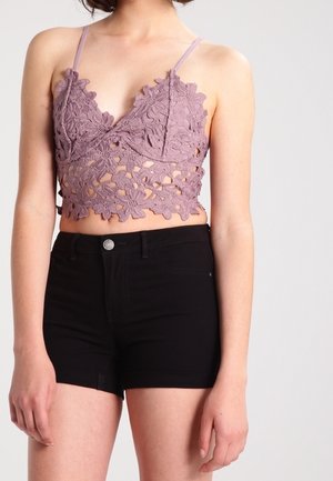 Kobieta nosząca malwowy koronkowy crop top w kwiaty z cienkimi ramiączkami i czarne szorty z wysokim stanem na jednolitym tle.