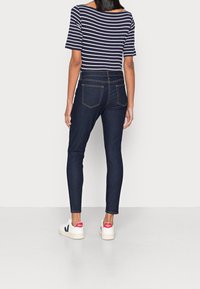 Camiseta de rayas marinas con mangas cortas, combinada con unos jeans ajustados azul oscuro y zapatillas blancas con acentos rojos. Tejido suave y corte ajustado.