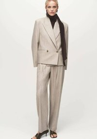 Traje gris claro a rayas con chaqueta de doble botonadura y pantalones de pierna ancha. Acompañado de un suéter de cuello alto oscuro y chal.