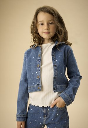 Kurtka dżinsowa z ozdobami z pereł, w niebieskim kolorze, o krótkim kroju, zapinana na guziki, zestawiona z białym prążkowanym topem i dopasowanymi dżinsami.