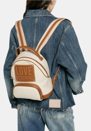Person wearing distressed blue denim jacket and jeans, carrying small cream and brown backpack with "LOVE MOSCHINO" logo on back.