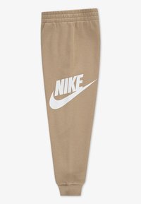 Pantalons de sport beiges avec des poignets côtelés à la cheville, une taille élastique et un grand logo Nike blanc imprimé sur la jambe gauche.