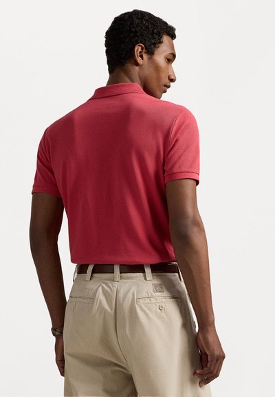 Κόκκινο πόλο μπλουζάκι με υφή πλέξης, κοντά μανίκια και γιακά, σε συνδυασμό με μπεζ παντελόνια και καφέ ζώνη.