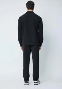 Chemise noire à boutons, coupe droite, associée à un pantalon noir assorti ; tissu lisse ; design épuré ; portée avec des chaussures de sport.