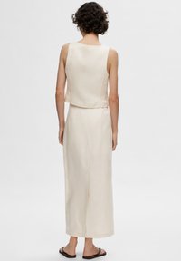 Lys beige, ærmeløs kjole med en tætsiddende overdel og en flagrende nederdel. Glat tekstur og længde til midten af læggen med en slids i ryggen. Minimalistisk design.