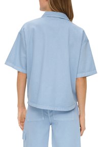 Light blue, short-sleeve, collared denim shirt with a relaxed fit. The fabric appears smooth with visible stitching and a straight hemline.