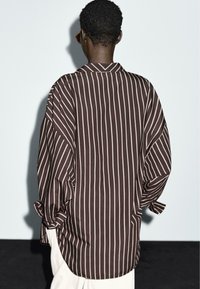 Bruine en witte gestreepte shirt met een relaxte pasvorm, voorzien van een kraag en opgerolde mouwen. Gemaakt van lichtgewicht stof, met een soepele textuur.