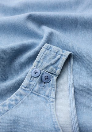 Primo piano di tessuto di denim azzurro con una cinghia piegata fissata da due bottoni blu abbinati.