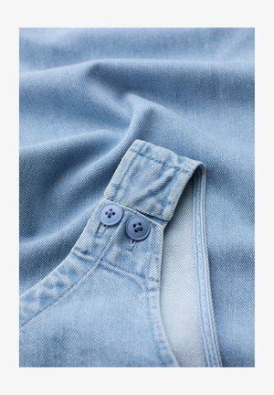 Close-up van lichtblauwe denimstof met een gevouwen band vastgemaakt met twee bijpassende blauwe knopen.