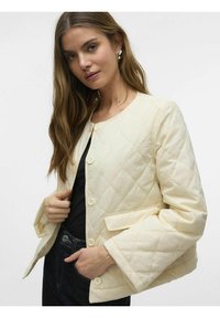 Chaqueta acolchada de color crema con cuello redondo, botones a presión y un bolsillo de parche. Presenta mangas amplias y un tejido texturizado.