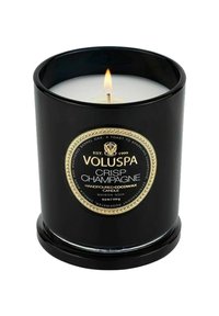 Voluspa Crisp Champagne kynttilä mustassa lasiastia. Valkoinen vaha, kultainen etiketti ja häilyvä liekki keskellä. Käsin kaadettua kookosvahaa.