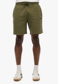Pantalones cortos de algodón verde oliva con cintura elástica y cordón. Cuenta con bolsillos laterales y un pequeño logotipo en el dobladillo.