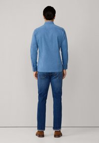 Lichtblauw overhem shirt gemaakt van zachte stof, met lange mouwen, een kraag en dichtgeknoopte manchetknopen, gecombineerd met donkerblauwe jeans en bruine schoenen.