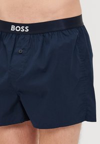 Şorturi de baie bleu marin, realizate dintr-un material ușor, având un brâu elastic cu logo-ul "BOSS" și un detaliu cu button în față.