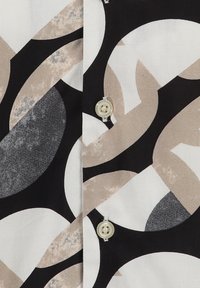 Blusa abotonada con un patrón geométrico de formas negras, beige y grises sobre un fondo blanco; incluye un pequeño botón redondo de color crema.
