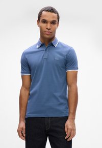 Polo shirt bleu avec une patte de boutonnage à trois boutons et un col avec une bordure blanche. Le matériau semble lisse et ajusté, avec un petit logo brodé sur la poitrine.