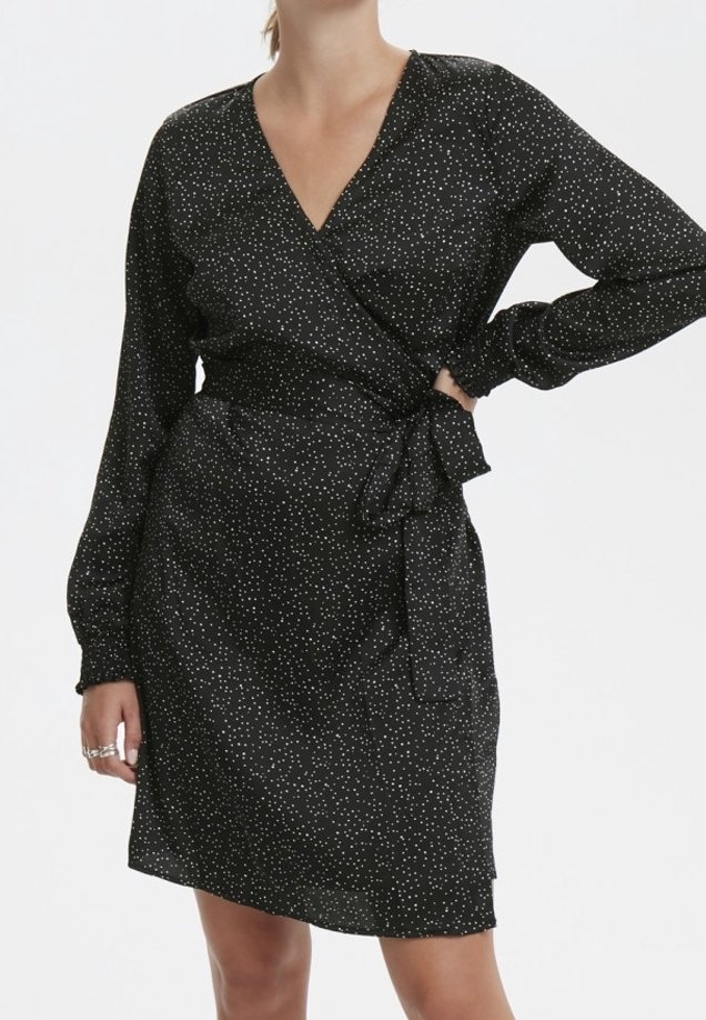 Vestido negro de envoltura con estampado de puntos blancos, mangas largas y un lazo en la cintura. Fabricado en material ligero, con un escote en V profundo.