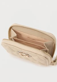 Μπεζ καπιτονέ πορτοφόλι κατασκευασμένο από υφή δέρμα, με χρυσό φερμουάρ, ροζ επένδυση εσωτερικά και διακοσμητική μεταλλική λεπτομέρεια στη μπροστινή πλευρά.