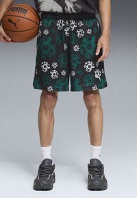 Pantalones cortos de baloncesto de malla negros con patrones de calaveras florales en verde y blanco, cinturilla elástica y bolsillos laterales. Combinados con zapatillas grises.