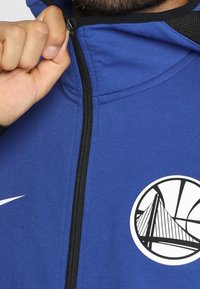 Sudadera con capucha azul con cremallera negra y forro de malla, con un gráfico blanco de baloncesto con un diseño de puente en el frente.