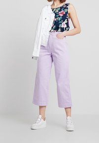 Kukkakuosiset hihattomat paidat tummansinisinä, yhdistettyinä laventelinvärisiin leveälahkeisiin housuihin ja valkoiseen farkkutakkiin, täydentäen asua valkoisilla lenkkareilla.