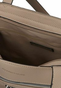 Interno di una borsa in pelle beige con un compartimento con cerniera, texture liscia e rivestimento in tessuto. Logo Tom Tailor visibile.