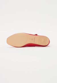 Zapato de tacón alto rojo con un acabado suave y brillante, punta redondeada y suela de goma marrón clara con ranuras sutiles y detalles de la marca.