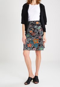 Jupe noire avec des broderies florales colorées comprenant des motifs verts, oranges et rouges. Associée à un t-shirt blanc et une veste courte noire.