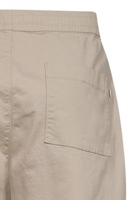 Beige, kevyt kangasvaate, jossa on joustava vyötärö ja yksi takatasku. Sujuva pinta hienovaraisella tikkauskoristelulla.