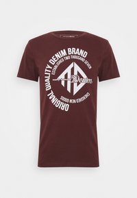 Camiseta de algodón color burdeos con un diseño gráfico circular que incluye texto blanco y un logo central, de mangas cortas y cuello redondo.