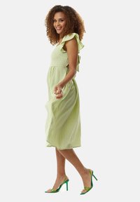 Green and white striped midi dress with ruffled shoulder detail, featuring cut-out sides. Paired with clear green high-heeled sandals.
