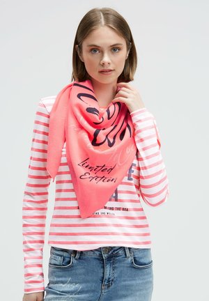Young woman with shoulder-length hair wears a pink striped long-sleeve shirt, denim jeans, and a bright coral scarf with black text "Limited Edition."