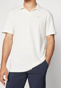 Cremefarvet polo T-shirt med korte ærmer, krave og et subtilt logo på brystet. Glat tekstur og afslappet pasform.