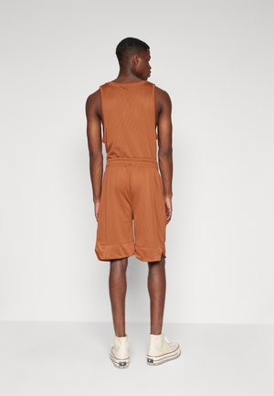 Set di top e pantaloni corti in rete color sabbia con vita elasticizzata, caratterizzato da una vestibilità comoda e una finitura testurizzata. Le calzature mostrano una sneaker in tonalità chiara.