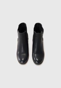 Botas de cuero negro hasta el tobillo con una textura suave, puntera redondeada y acentos laterales elásticos para facilitar su uso. Diseño minimalista, sin herrajes visibles.
