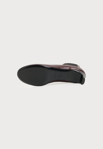 Vue de profil d'une chaussure habillée en cuir marron foncé avec une semelle noire lisse et un petit talon sur un fond clair uni.
