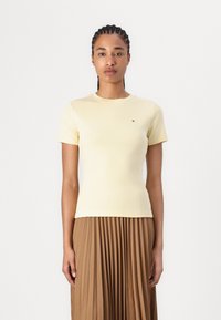 Yellow fitted t-shirt made of soft cotton, featuring short sleeves and a small logo detail on the chest, paired with a pleated brown skirt.