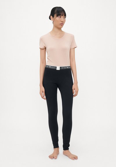 Persikofärgad t-shirt med kort ärm och rund halsringning, tillsammans med svarta stretchiga leggings med en kontrasterande märkesmidja.