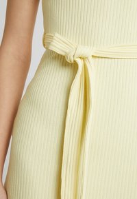 Gul ribbad kläddetalj med ett knytet tygbälte som betonar textur och form. Mjukt material med en slät, strukturerad design.