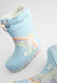 Botas azules impermeables con forro blanco esponjoso, que presentan diseños de arcoíris y sol, acentos de estrellas brillantes y una suela texturizada.