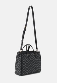 Black tote bag featuring a chevron pattern in grey, leather accents, dual handles, and an adjustable shoulder strap. Gold hardware details.