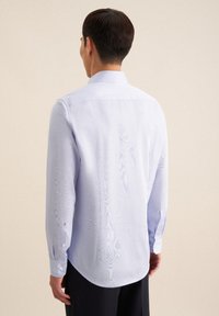 Lichtblauw overhemd van gladde stof. Heeft lange mouwen, een puntige kraag, knoopmanchetten en een ronde zoom.