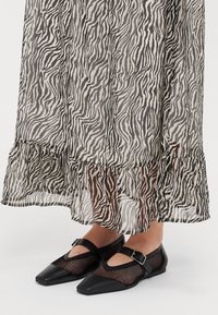 Svart och vit zebra-mönstrad genomskinlig kjol med volangkant, ihopparad med svarta ballerinas med spets och nätdesign samt rem.